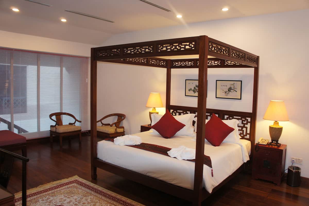A four-poster bed with white linens, red pillows, and a wooden headboard. There are two bedside tables with lamps and a small trash bin.