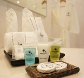 A tray with toiletries including shampoo, body lotion, and bath foam, along with towels and robes.