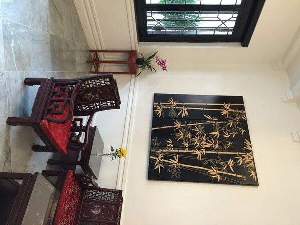 Una habitación con una silla de madera tradicional, una mesita con un florero y una obra de arte en la pared que representa bambú.