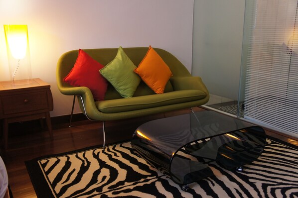 Una sala de estar moderna con un sofá verde, dos almohadas, un felpudo con estampado de cebra y una mesa de centro de vidrio.