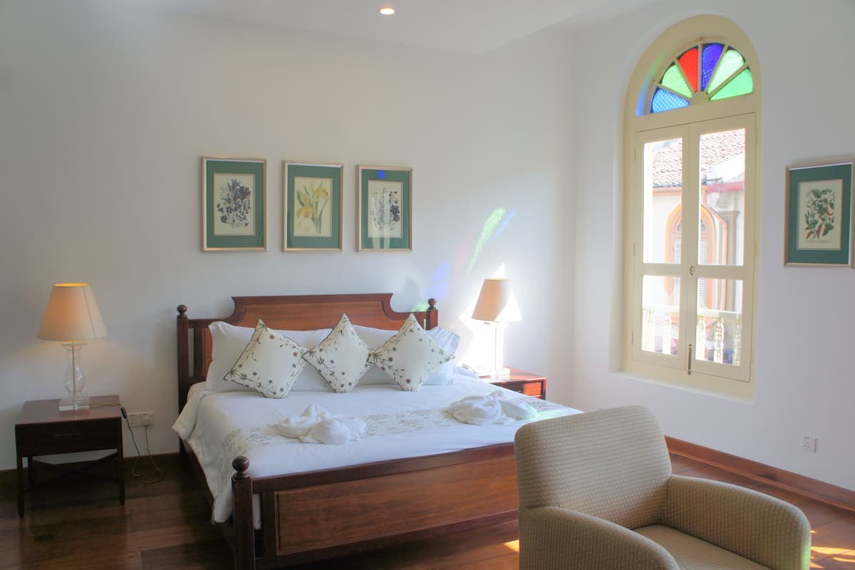 A neatly arranged bedroom with a wooden bed, a chair, and a window with a stained glass design.