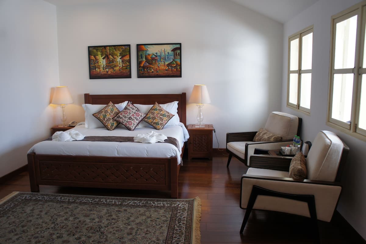 A bedroom with a large bed, two bedside tables, a chair, and two paintings on the wall.