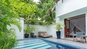 A pool area with steps leading into the water, surrounded by potted plants and a seating area with a table and chairs.