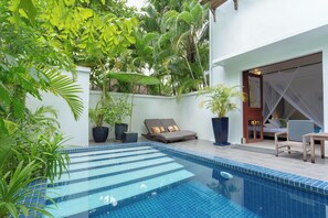 A pool area with steps leading into the water, surrounded by potted plants and a seating area with a table and chairs.