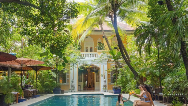 A pool area with a clear view of the pool, a covered seating area, and a building with a balcony in the background.