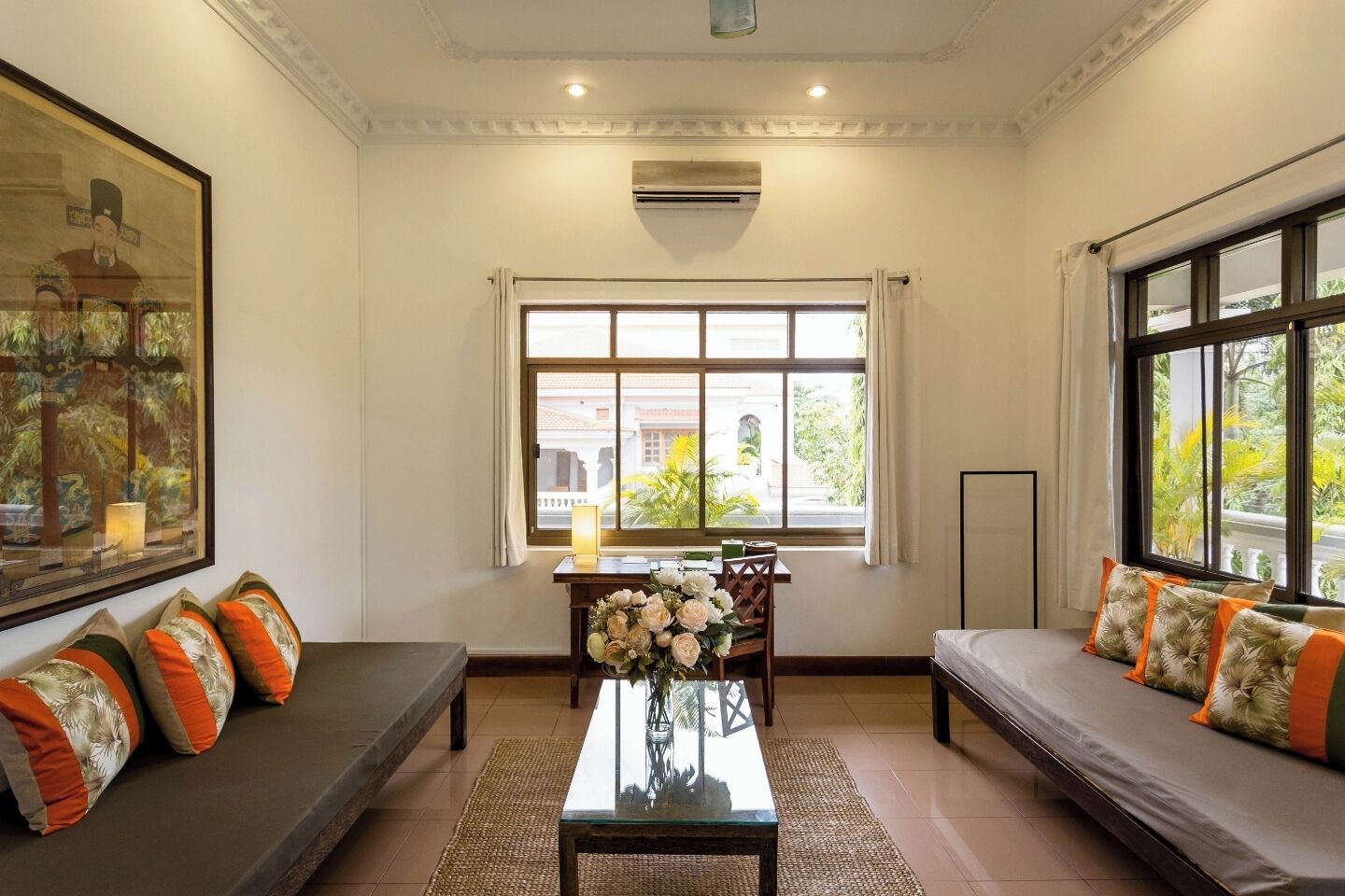 A room with a sofa, a dining table with chairs, a window with curtains, and a painting on the wall.