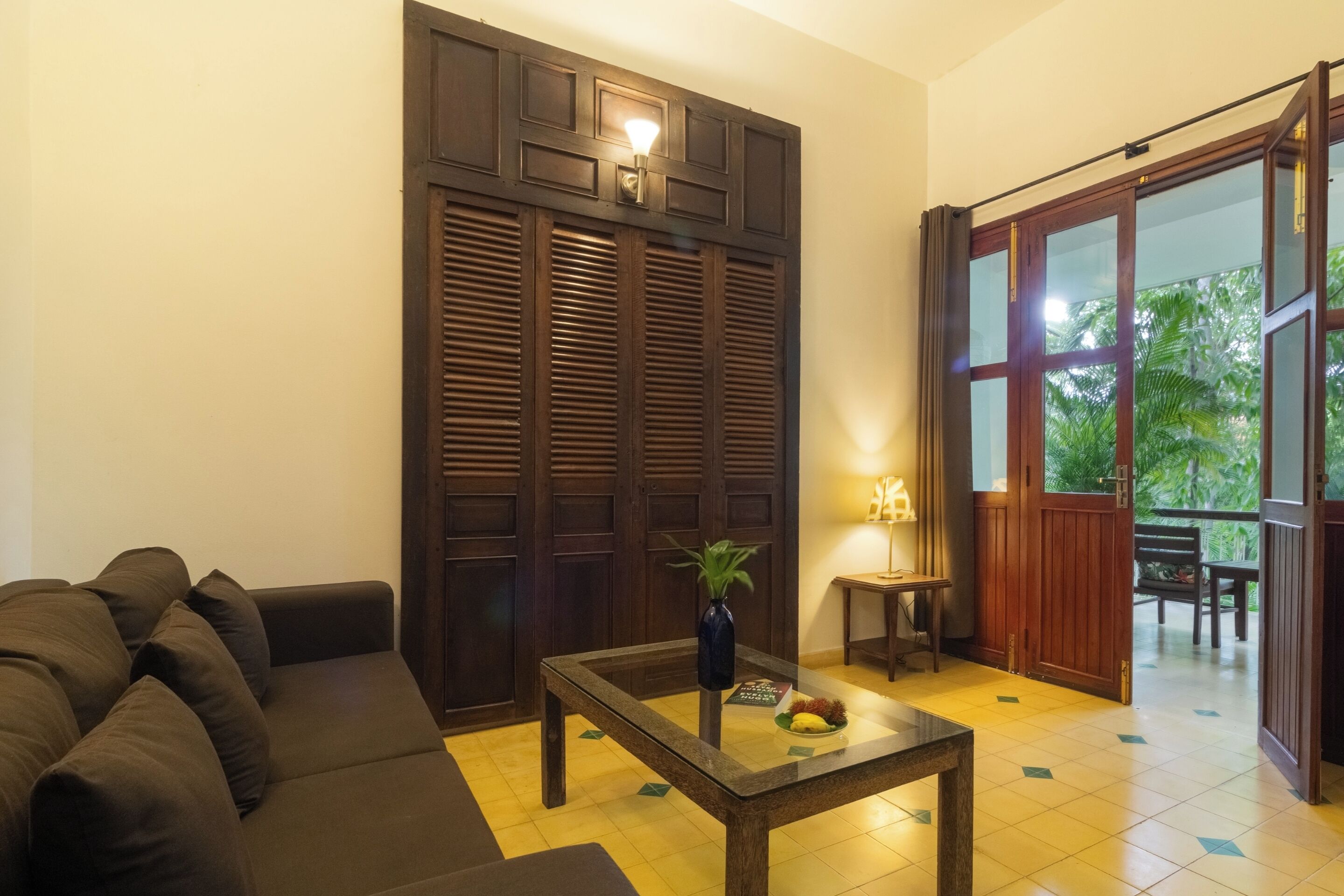 Un salón con sofá, una mesa de centro con una planta, una puerta de madera y vistas al exterior.