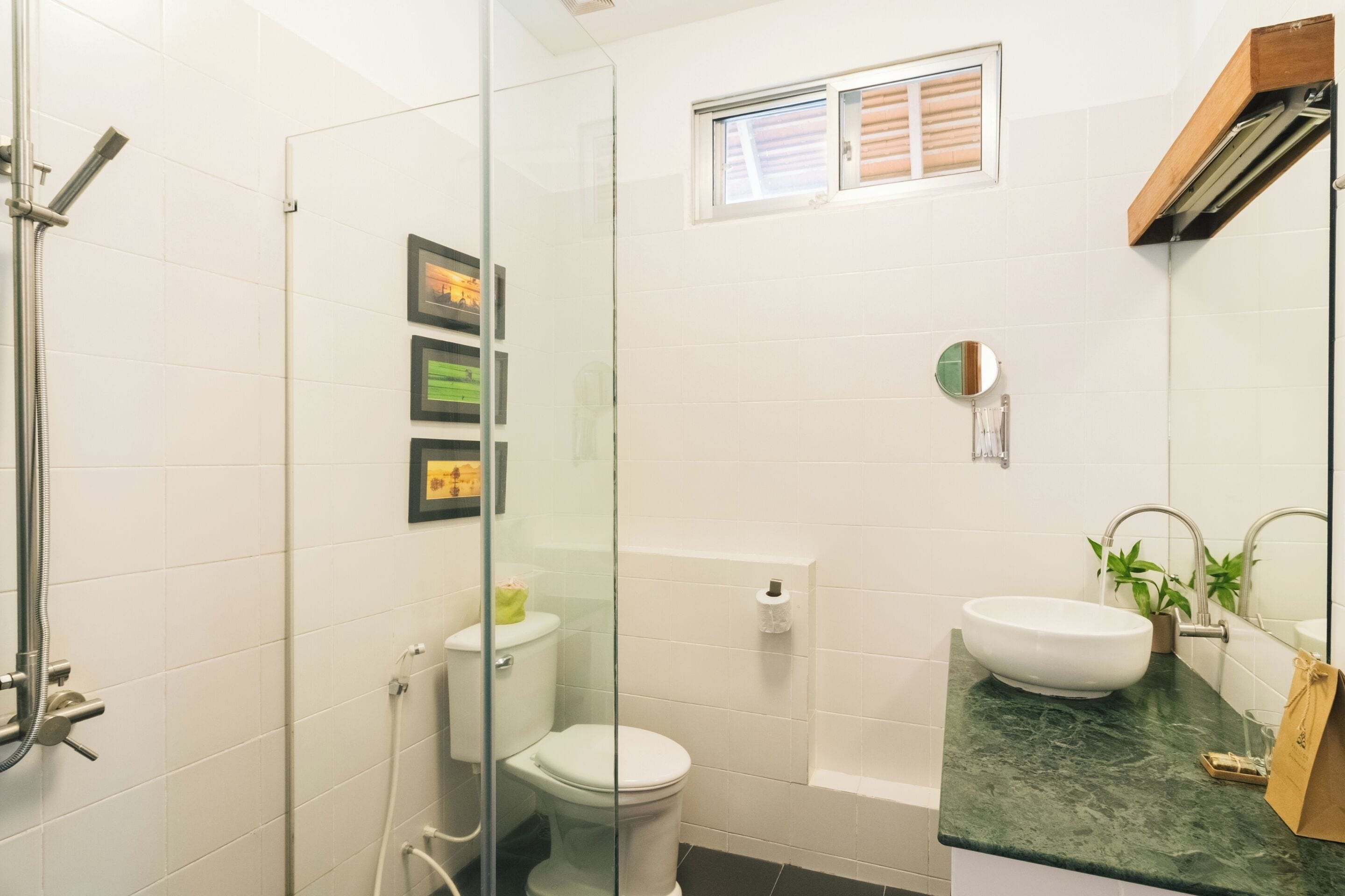 A bathroom with a glass shower enclosure, a toilet, a bathtub, a sink, and a small window.
