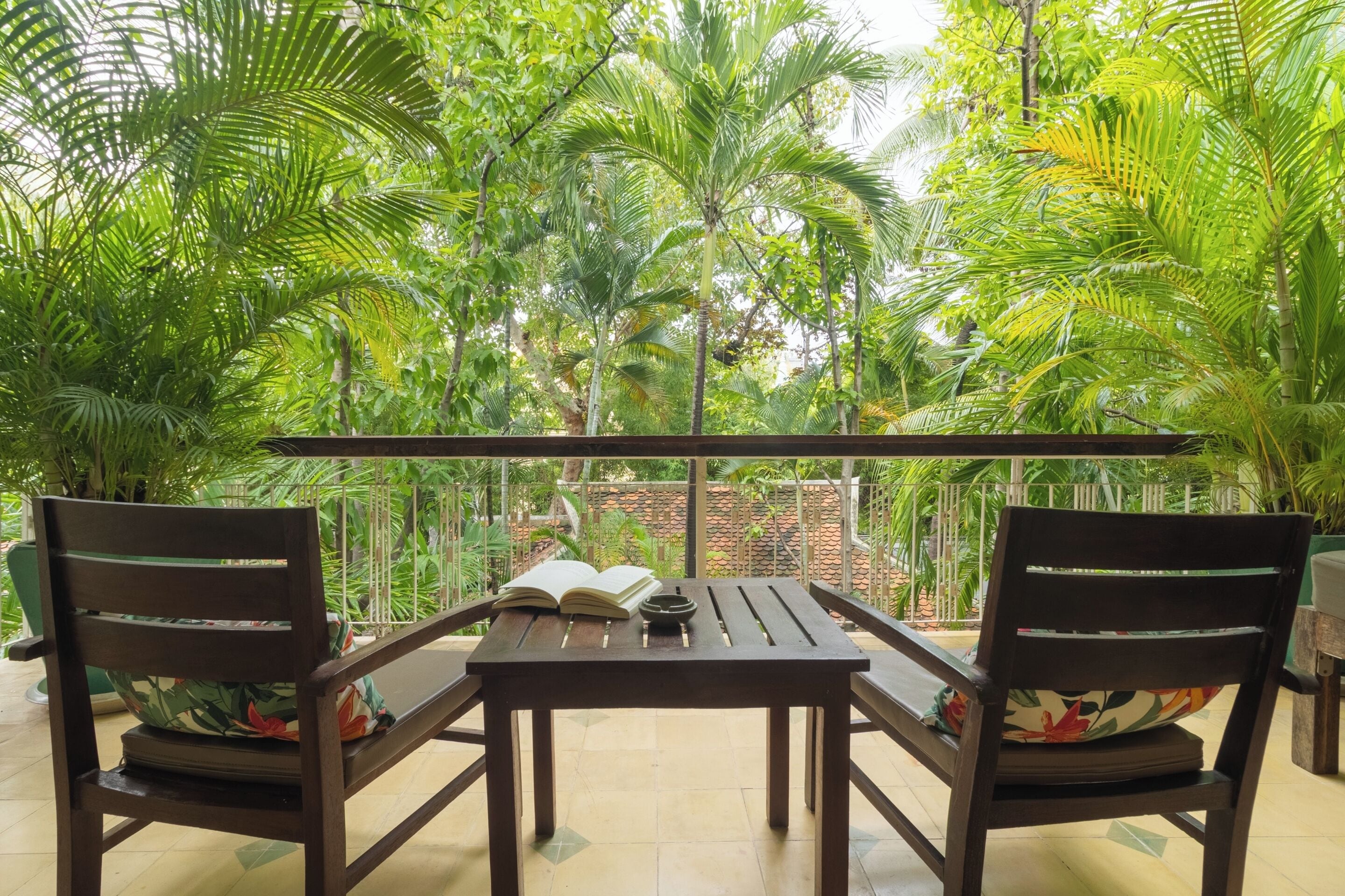 A wooden table with two chairs and an open book, surrounded by lush green foliage.