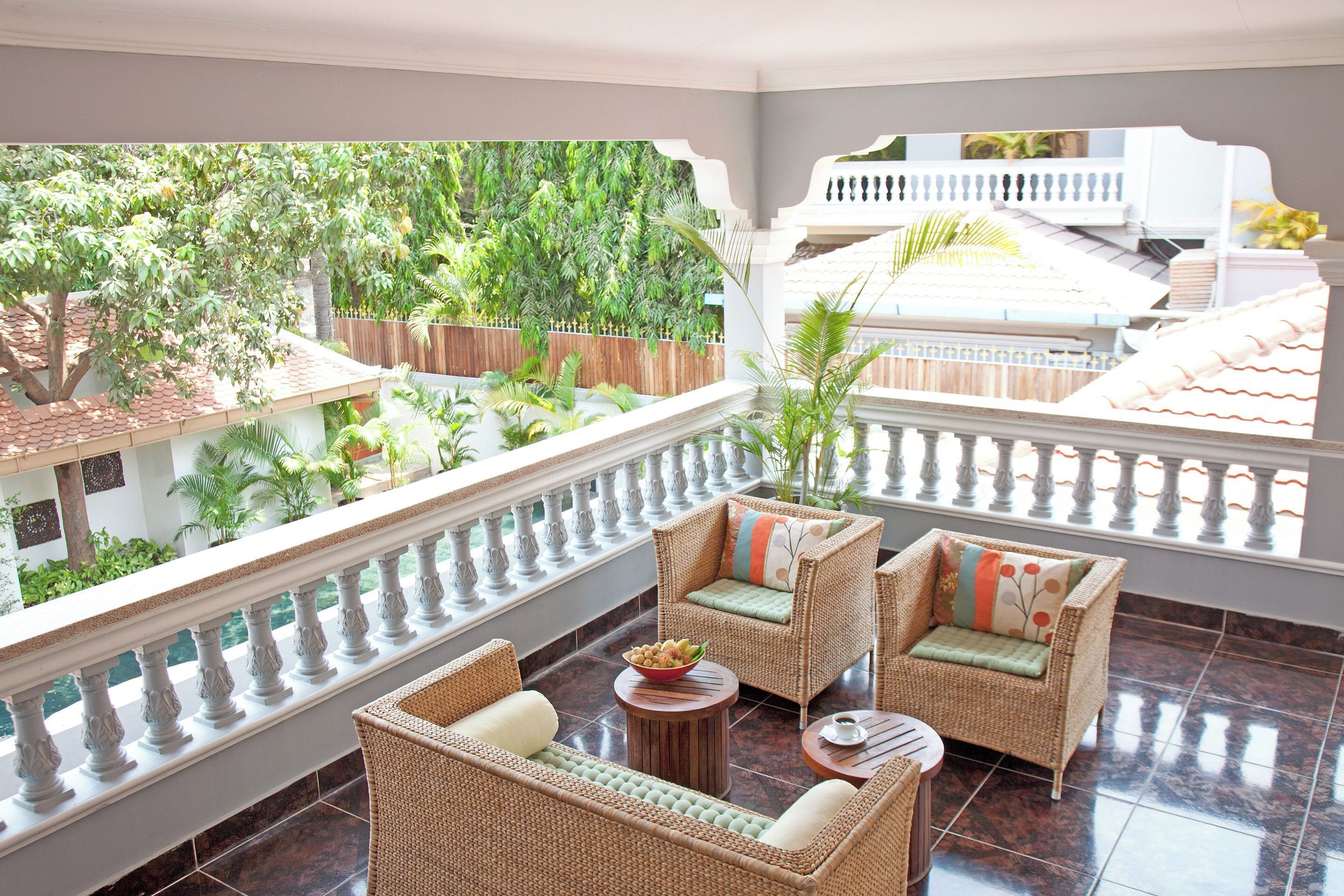 A balcony with wicker furniture, a small table, and a view of a lush garden.