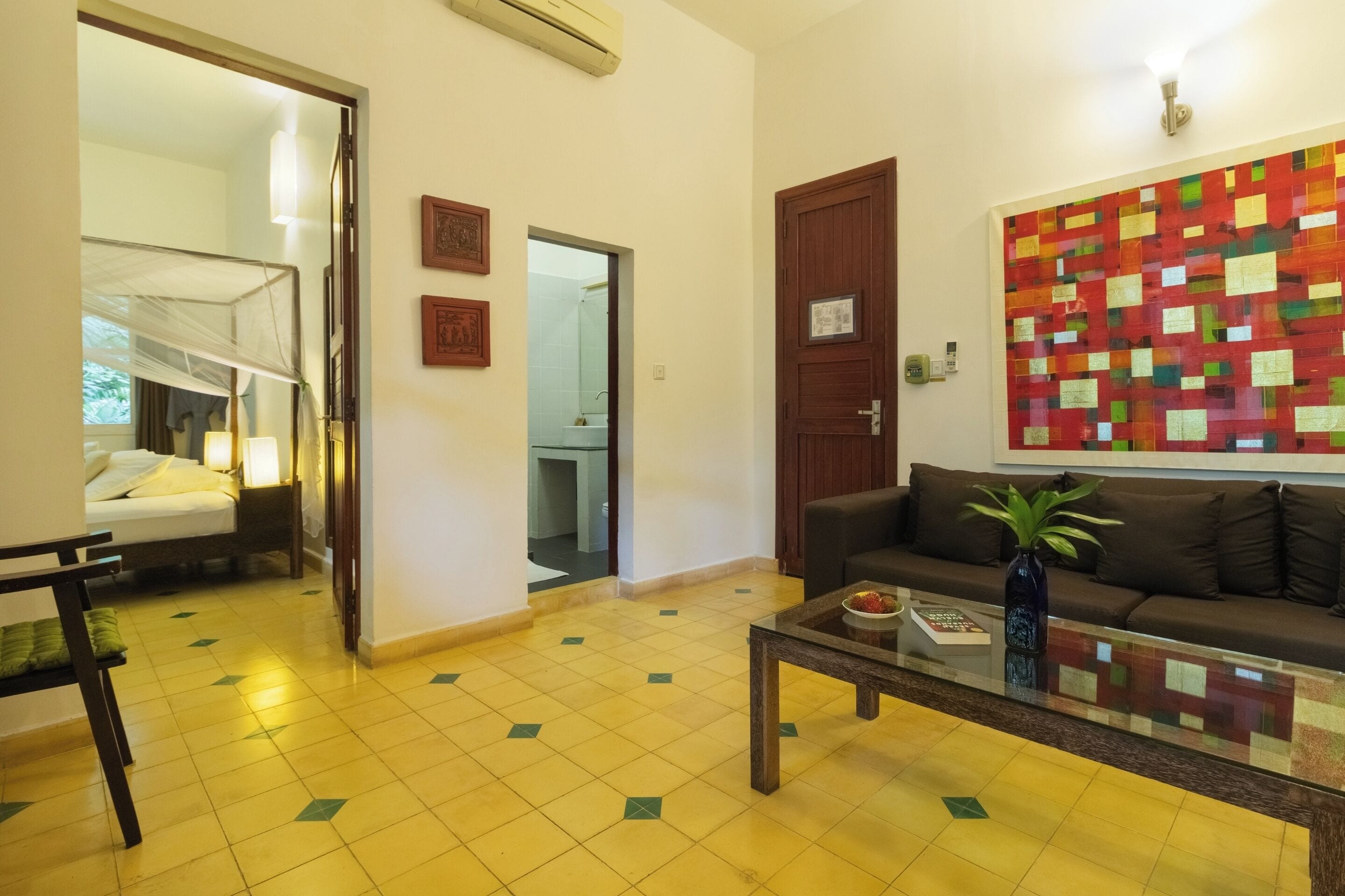 A hotel room with a bed, a sofa, a coffee table, and a colorful abstract painting on the wall.