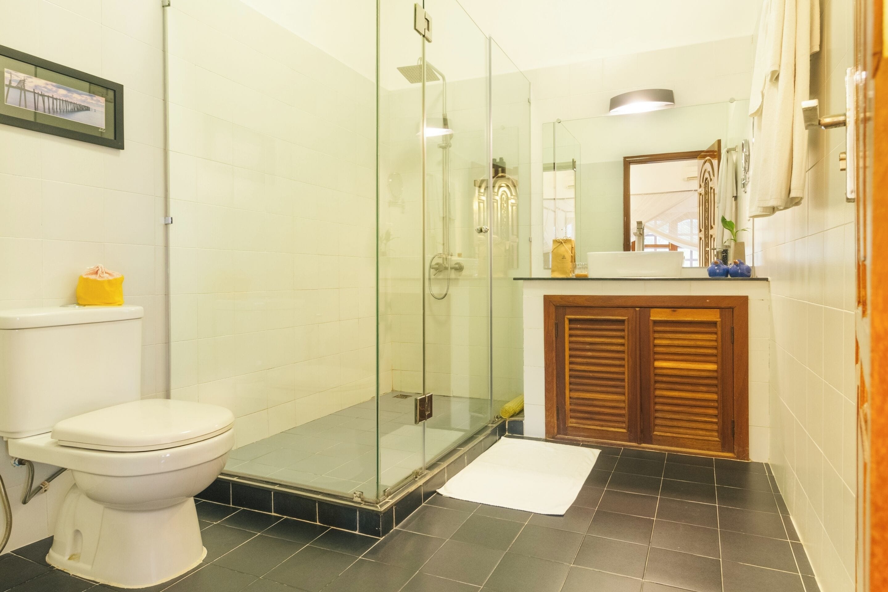 Une salle de bain comprenant des toilettes, une douche fermée par une paroi de verre, un lavabo avec un miroir et un meuble en bois.