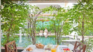 A dining table with breakfast items, a glass of orange juice, and a view of a pool and fountain.
