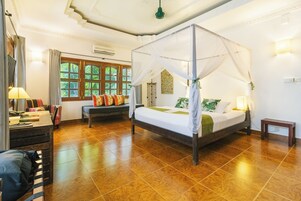 Een kamer met een hemelbed, een bureau met stoel, een raam met gordijnen en een wandairconditioner.