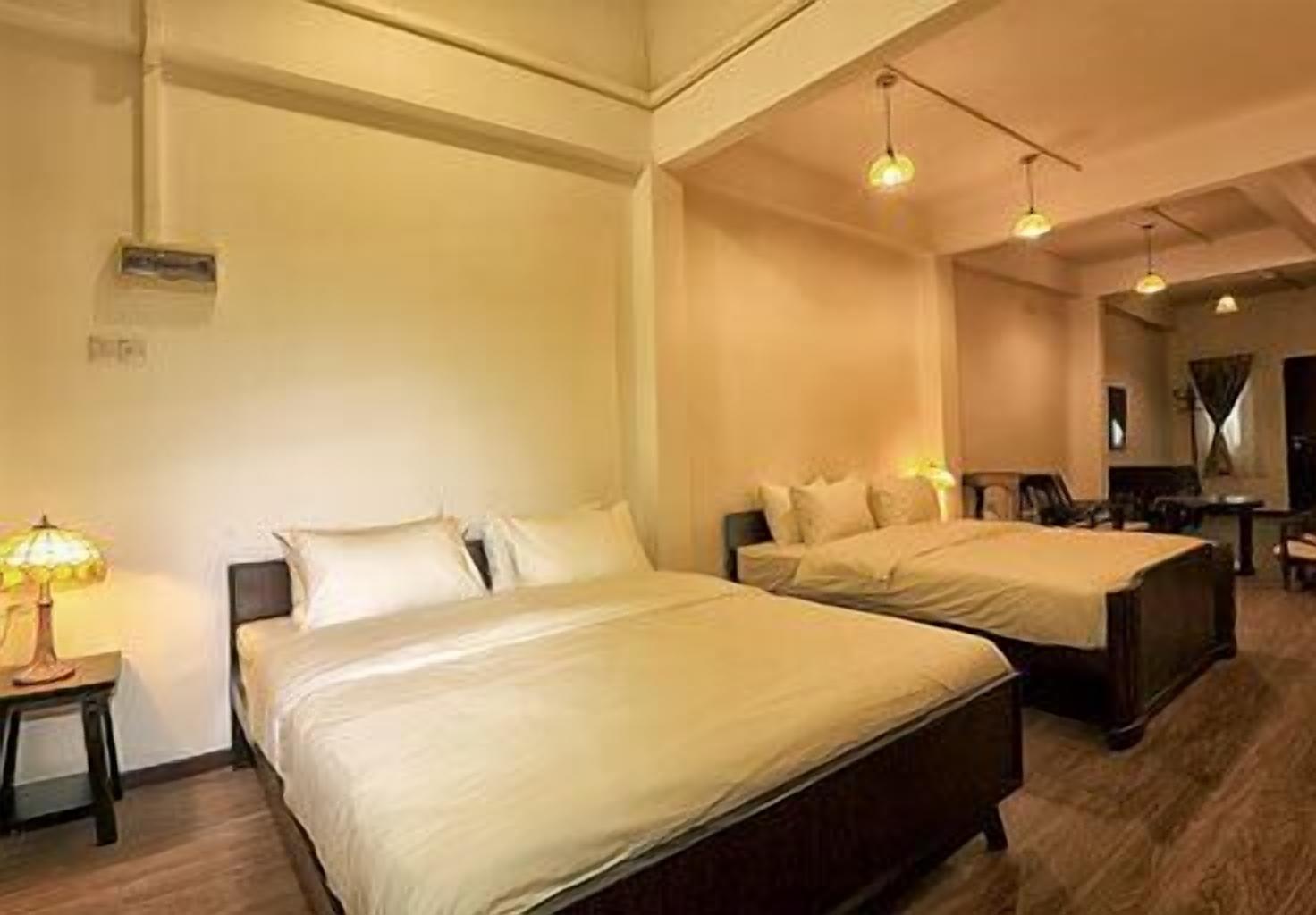 A hotel room with two beds, a nightstand, a lamp, and a desk with a chair.