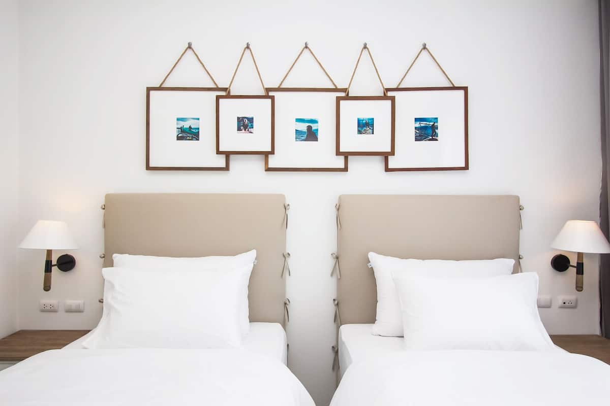 A hotel room with two beds, a beige headboard, white bedding, and a wall with framed pictures.