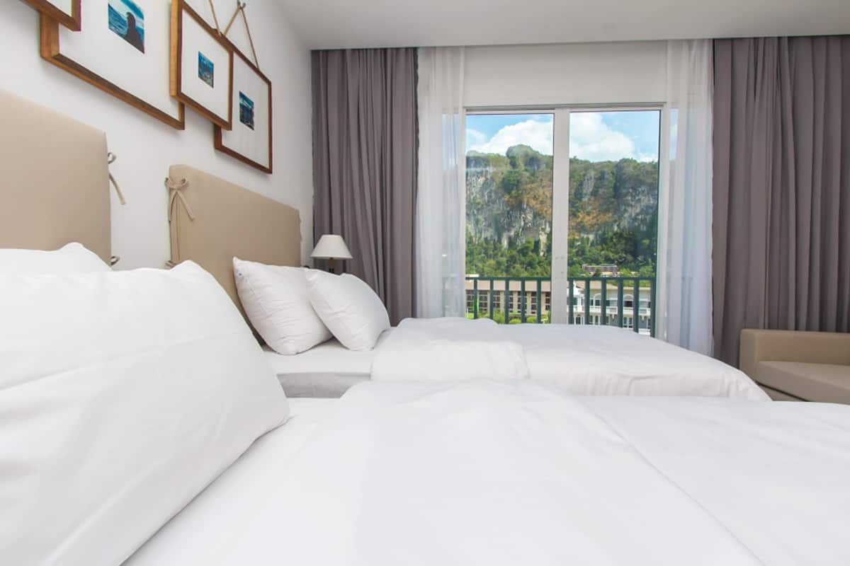 A hotel room with two beds, a balcony with a view of a mountainous landscape, and framed pictures on the wall.