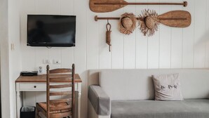 Een kamer met een flatscreen televisie, een houten bureau met stoel, een grijze bank en twee houten paddles aan de muur.
