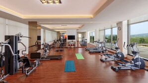 Une salle de sport spacieuse, dotée de divers équipements d’exercice, de grandes fenêtres et d’un design moderne.