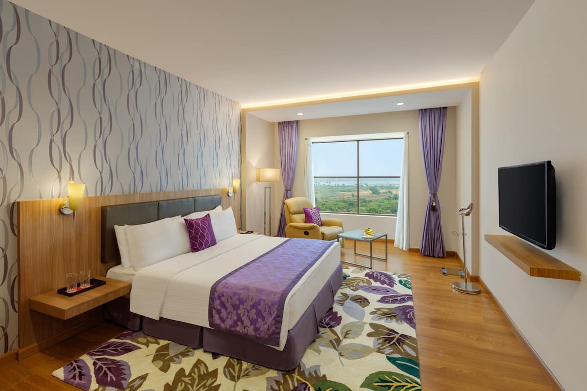 Una habitación de hotel moderna con una cama grande, televisor, escritorio con lámpara y vistas al exterior.
