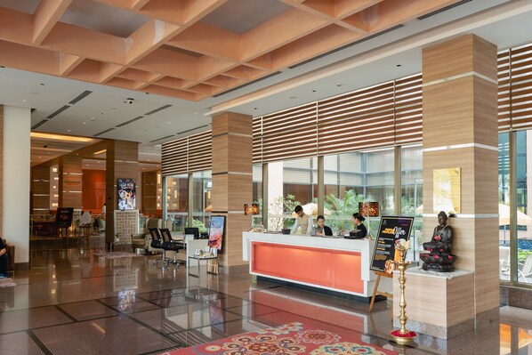 Un hall d’hôtel moderne avec un comptoir d’accueil, un espace salon et de grandes fenêtres.