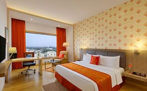 A hotel room with a large bed, a desk, a chair, a TV, and a view of the city. - Welcomhotel by ITC Hotels, GST Road, Chennai (Chengalpattu)