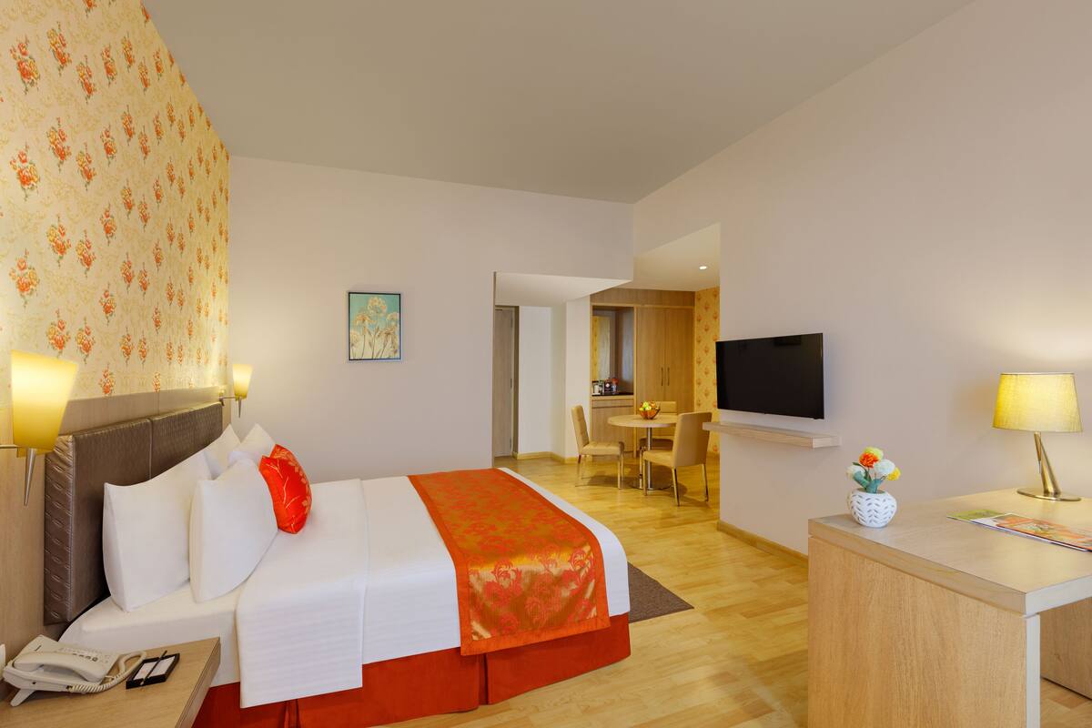 Habitación de hotel con cama, escritorio, televisor y zona de comedor.