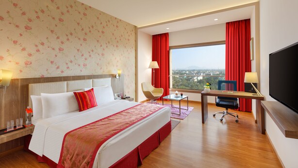 Une chambre d’hôtel avec un grand lit, un bureau avec une chaise, une télévision et une fenêtre donnant sur la ville.