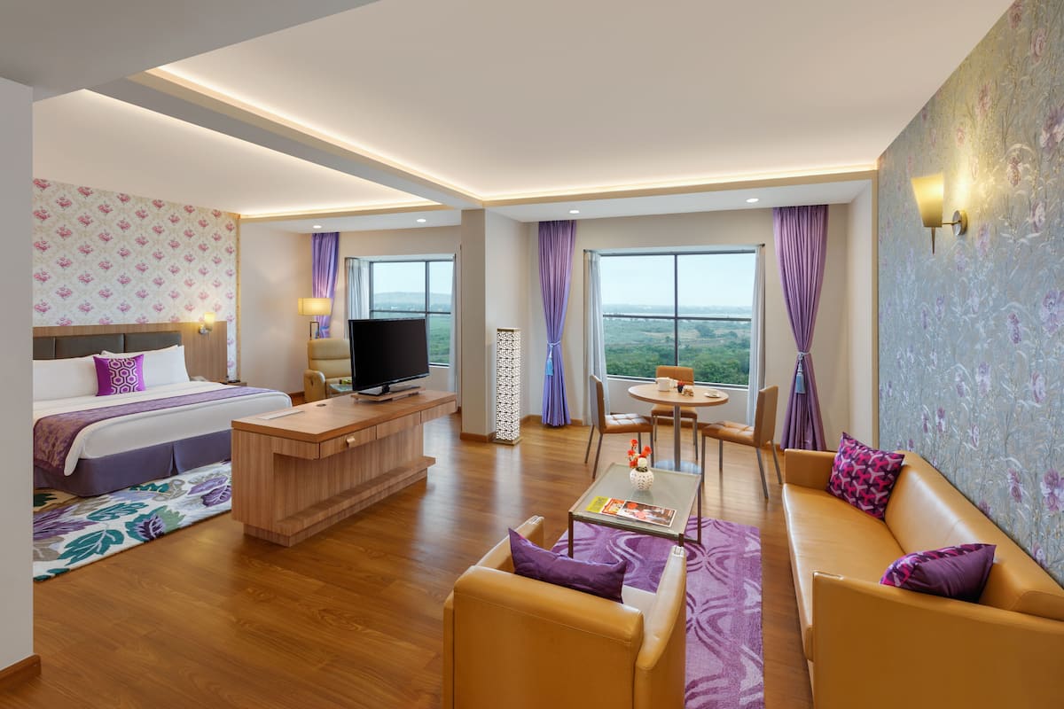 Una habitación de hotel moderna con cama, televisor, escritorio, sofá y zona de comedor con vistas.