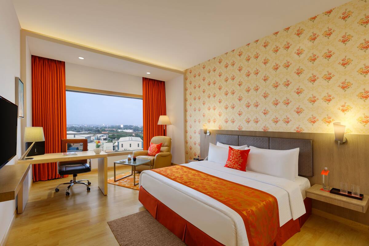 Habitación de hotel con una cama grande, un escritorio, una silla, un televisor y vistas a la ciudad.