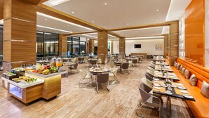 Un vaste espace de restauration dans l’hôtel, avec de nombreuses tables et un long comptoir où sont présentés les plats et les boissons.