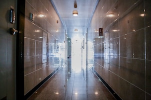 A corridor with reflective tiled walls and a polished floor, leading to a bright exit.
