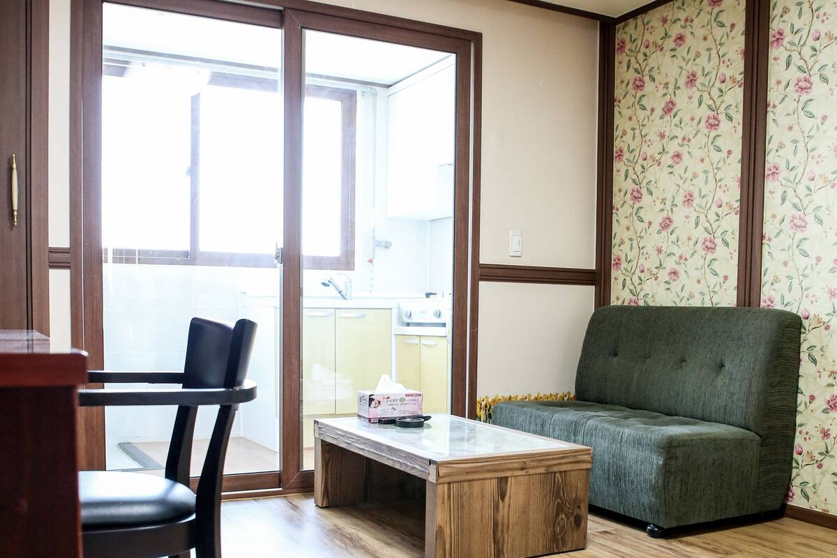 A living room with a wooden floor, a green sofa, a wooden coffee table, and a black chair.