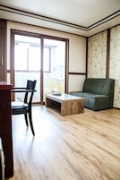 Una sala de estar con piso de madera, un sofá verde, una mesa de centro de madera y una silla negra.