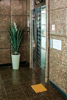 A lobby with a potted plant, a tiled floor, a sign with a wheelchair symbol, and a door leading to an elevator.