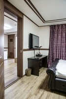 A hotel room with a bed, a desk with a computer, a television, and a bathroom visible through an open door.