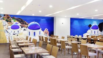 Un espace repas avec des tables et des chaises, une fresque murale bleue et un plafond blanc.