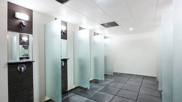 Uma fileira de sanitários públicos modernos, bem iluminados, com divisórias de vidro e piso ladrilhado.