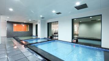 A modern indoor swimming pool with clear water, surrounded by a tiled floor and walls, and equipped with overhead lighting.