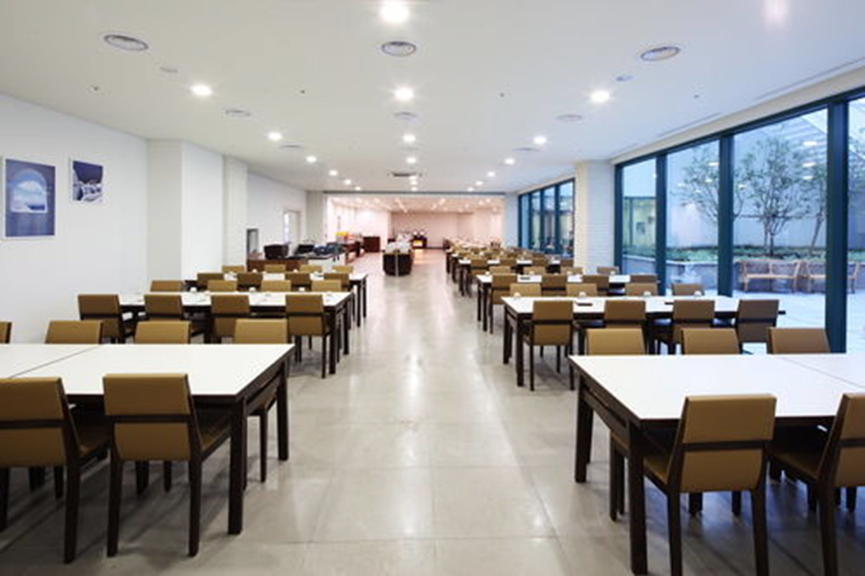 Uma sala de conferências ampla, com mesas e cadeiras compridas, janelas grandes e um design moderno no teto.