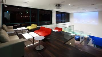 A modern lounge area with seating, a glass partition, and a projection screen.