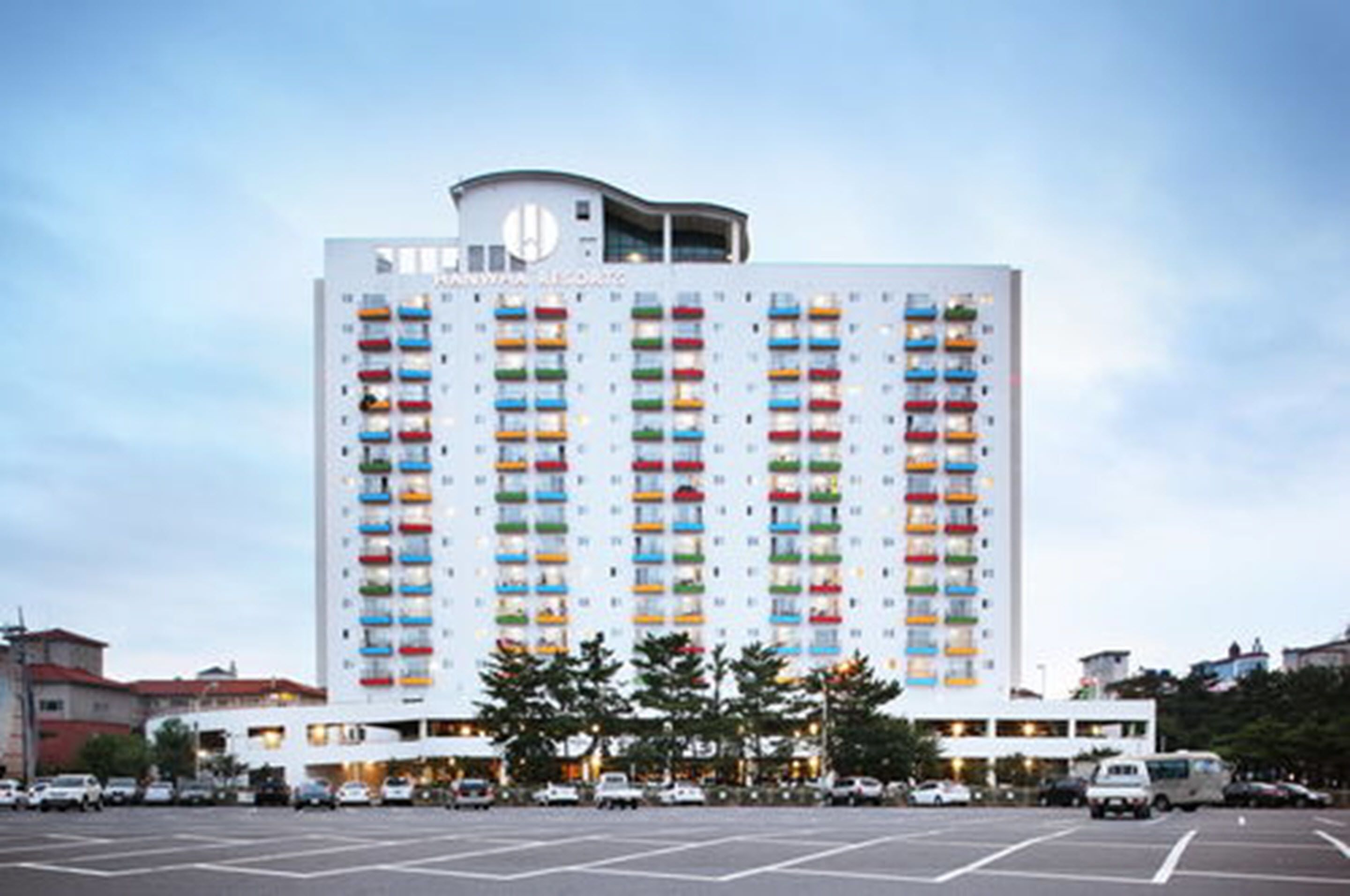 Ett högt hotell med flera balkonger, en central innergård och en parkeringsplats framför.