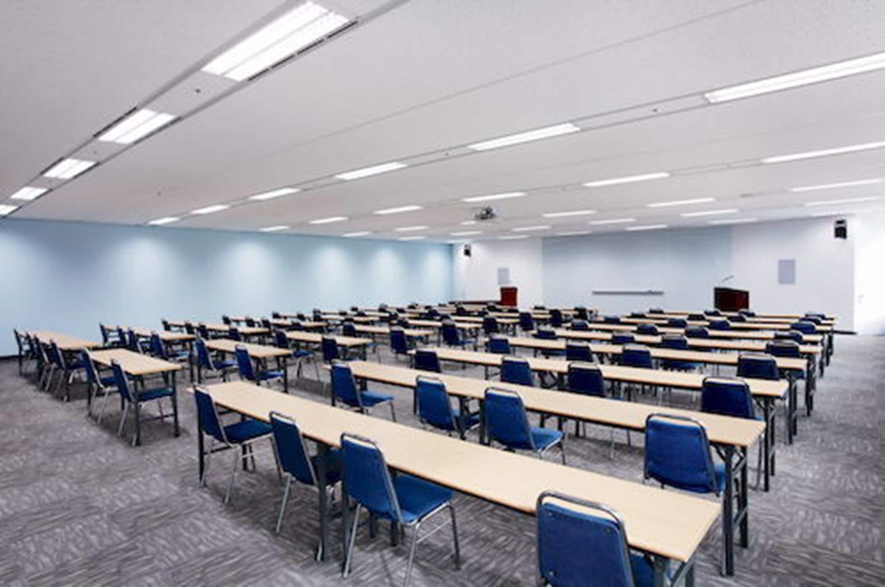 A classroom with rows of desks and chairs, a projector screen, and a podium.