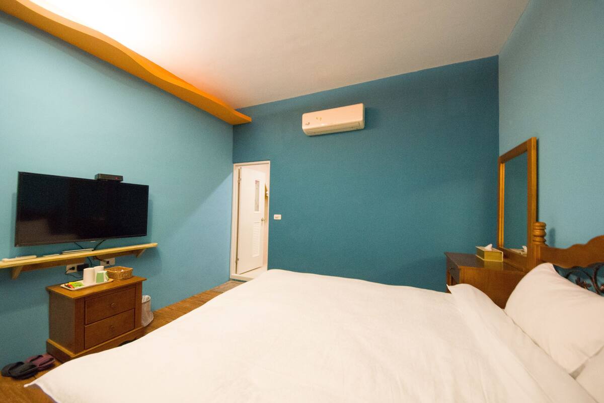 Habitación de hotel con cama, televisor sobre un mueble, cómoda, espejo y equipo de aire acondicionado.