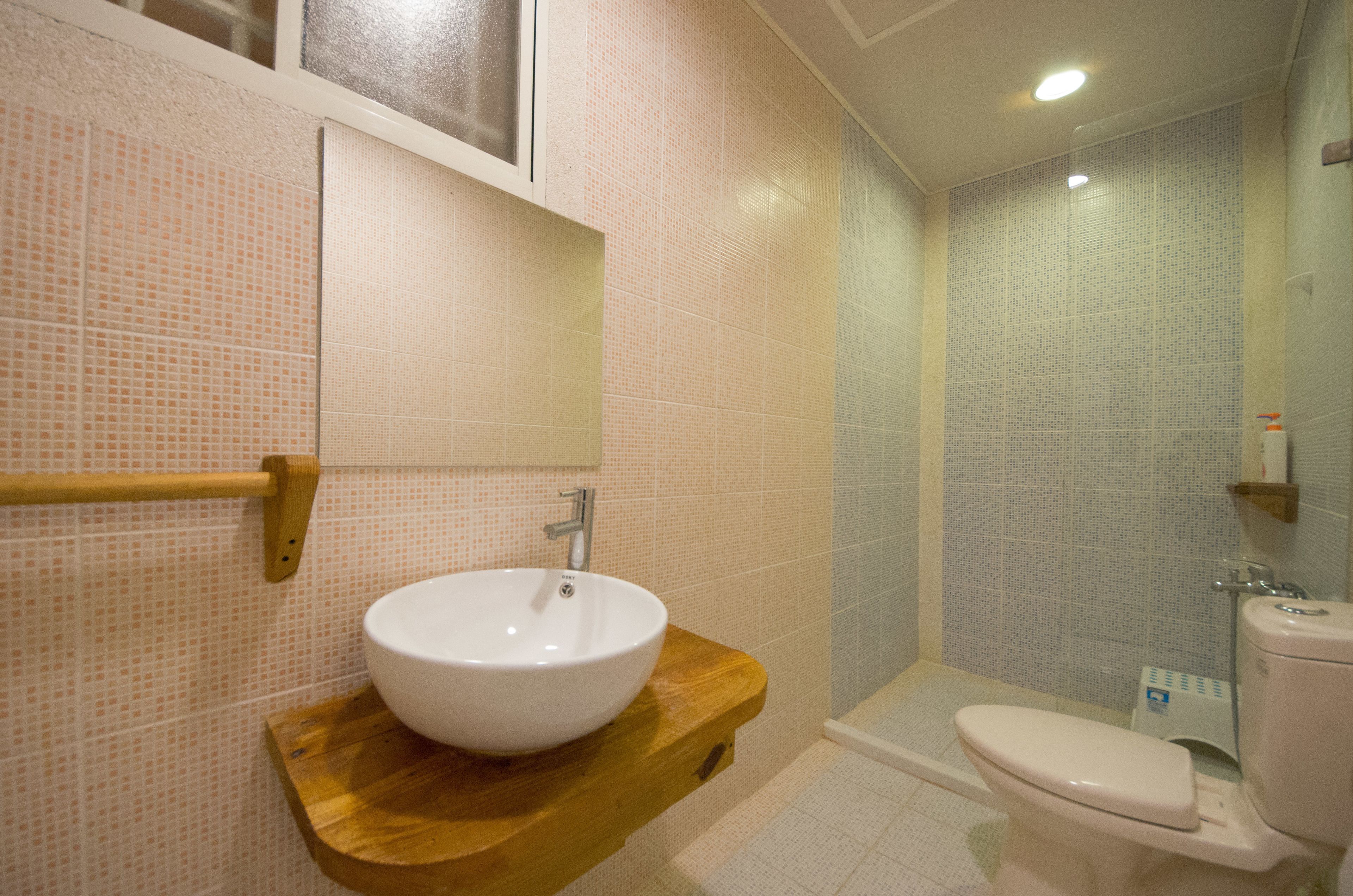 A bathroom with a wooden vanity, a white sink, a toilet, and a shower area.