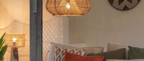 A cozy living room with a sofa, cushions, a table with candles, and a hanging light fixture.