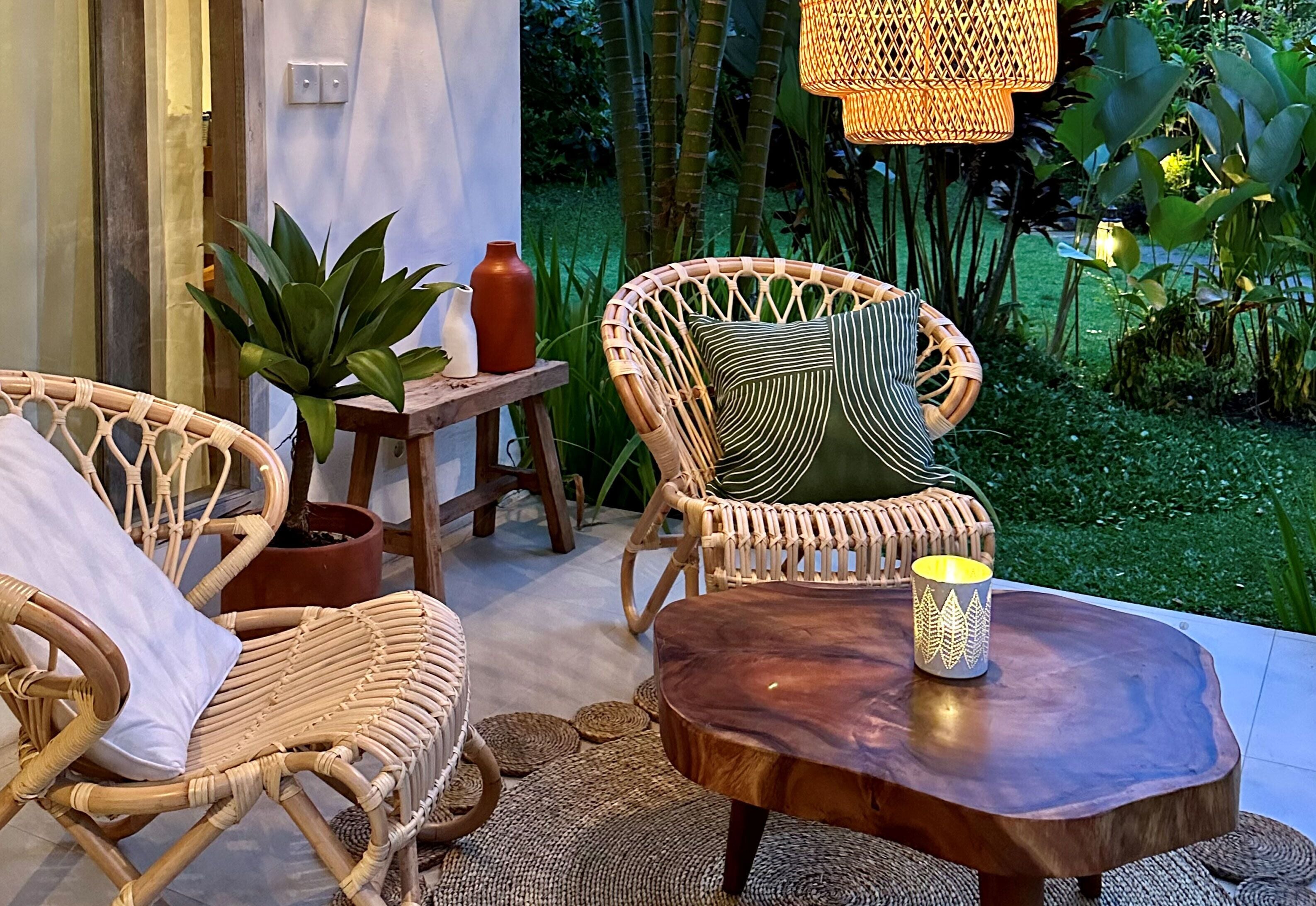 Une chaise en osier avec un coussin, une petite table en bois avec une bougie et une plante en pot.