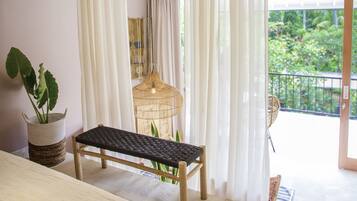 Una habitación con un banco de madera, una cesta de mimbre con plantas y una lámpara colgante, además de vistas al verde exterior.