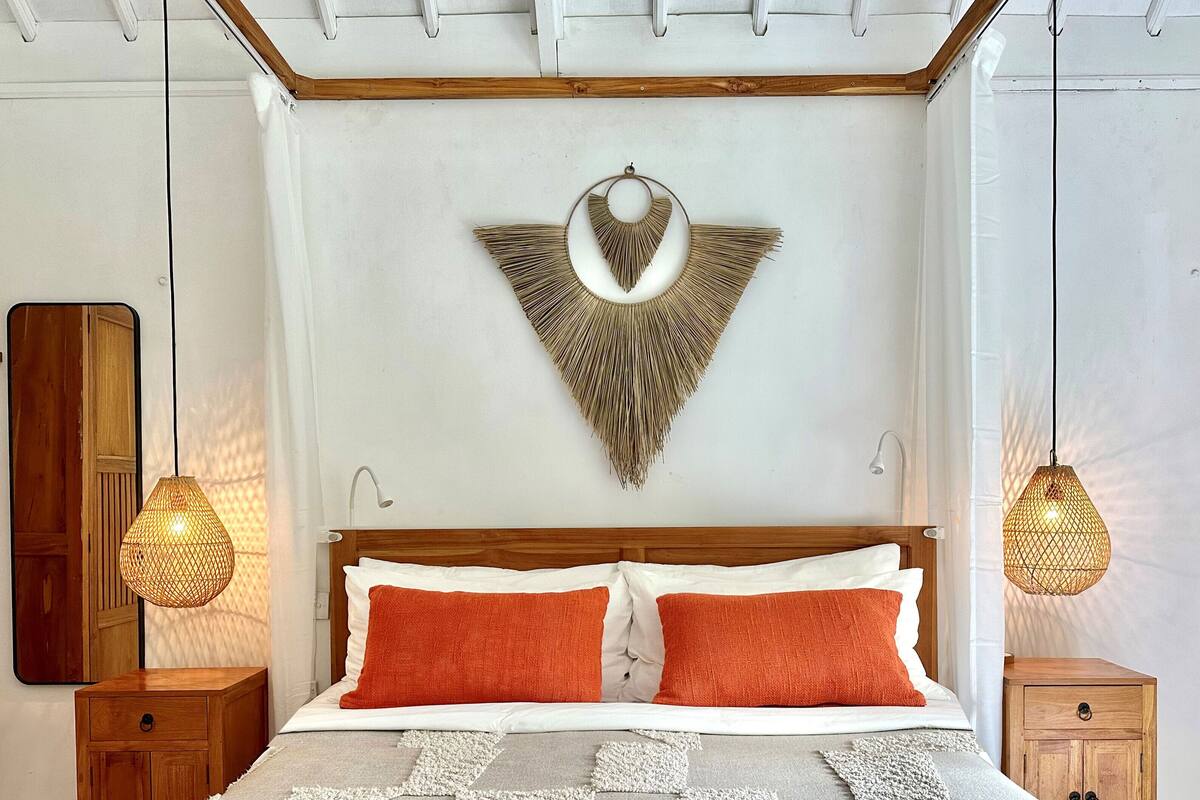 A bedroom with a wooden bed, two nightstands, a wall-mounted decorative piece, and two hanging lamps.