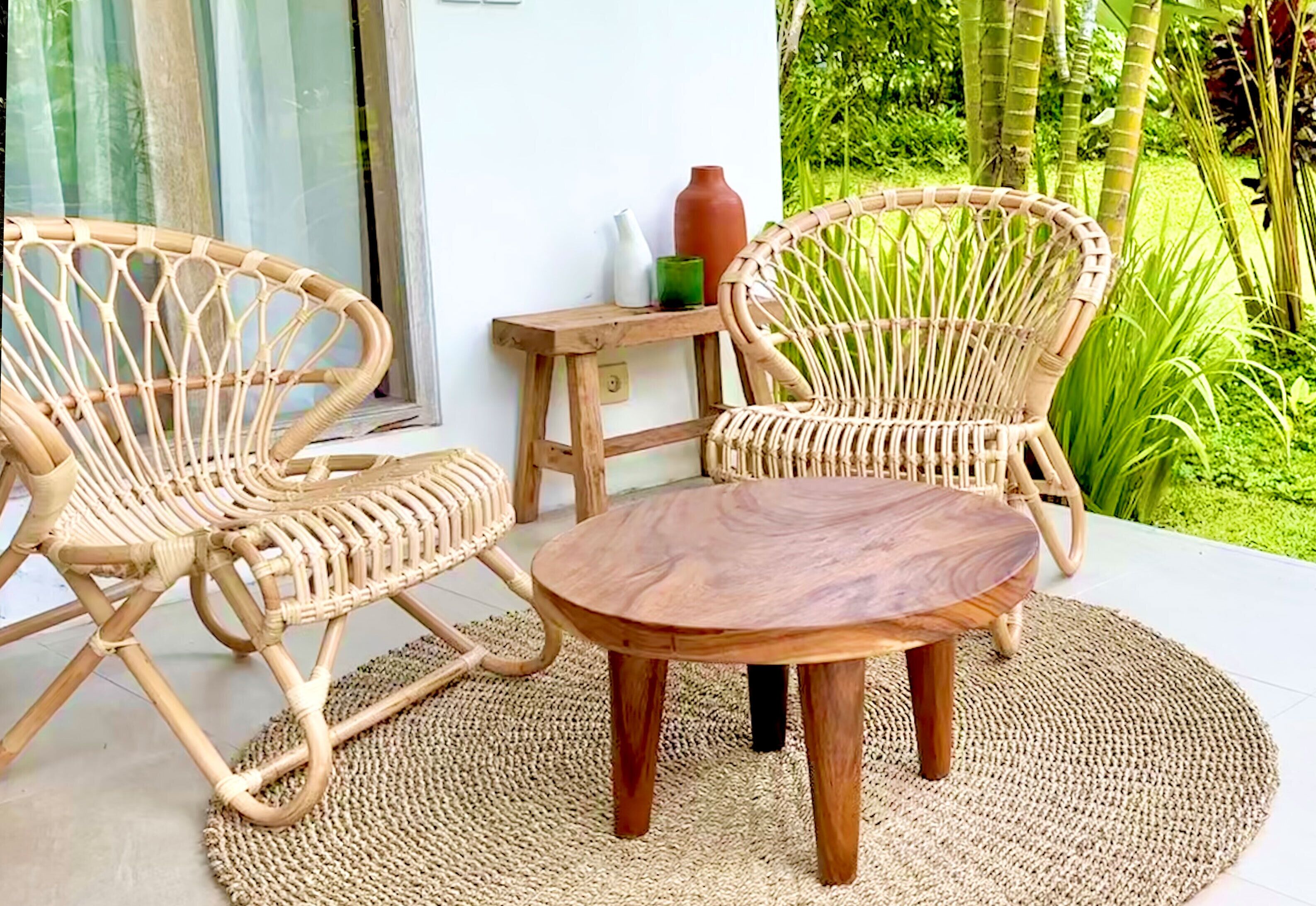 A wicker chair and table set on a woven mat, with a small wooden table beside them.